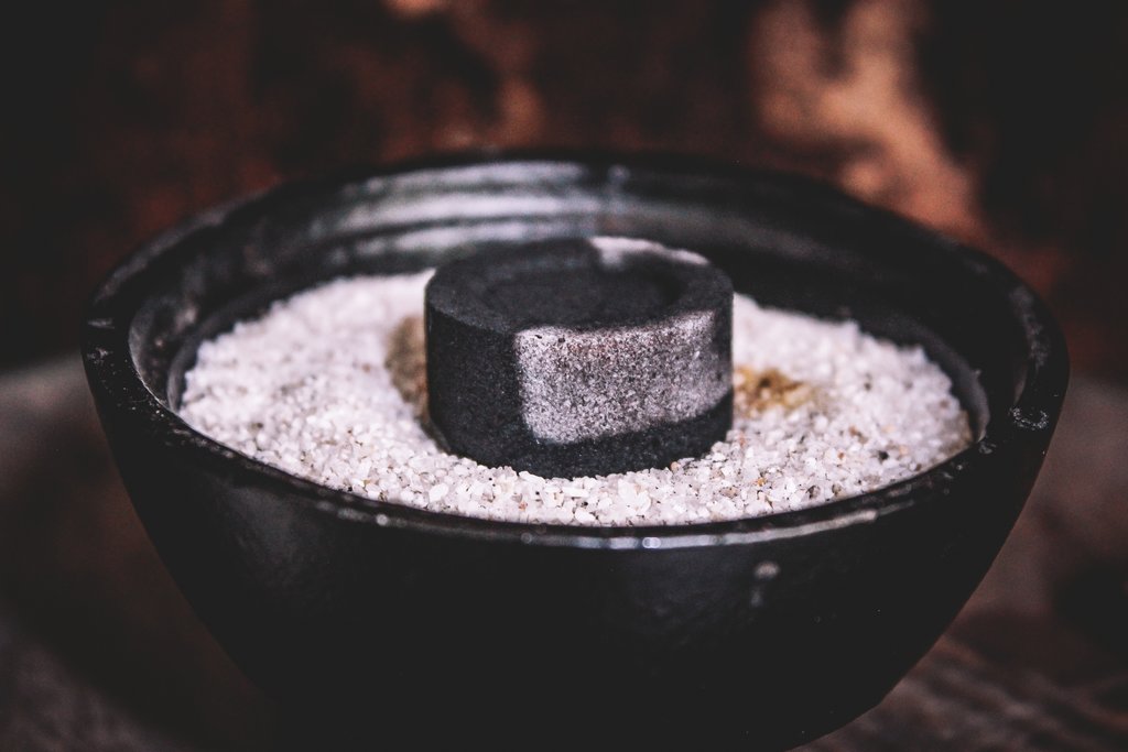 Ein Stück Räucherkohle auf weißem Sand in einem gußeisernen Gefäß.