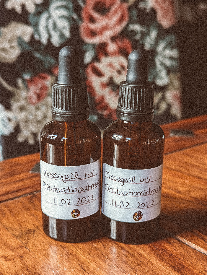 Zwei Pipetten-Flaschen aus Braunglas mit einem weißen Etikett auf dem steht: Massageöl bei Menstruationsschmerzen 11.02.2022