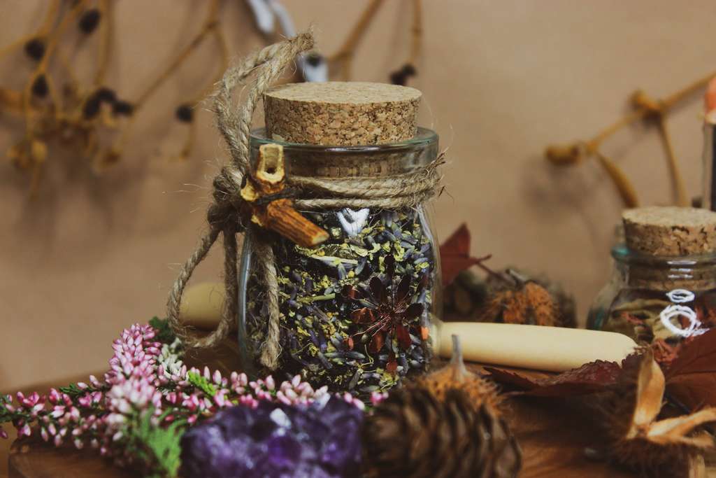 Ein Korkenglas mit Kräutern darin. Um das Glas herum gebunden ist eine Juteschnur und ein Stück Holz befindet sich daran.